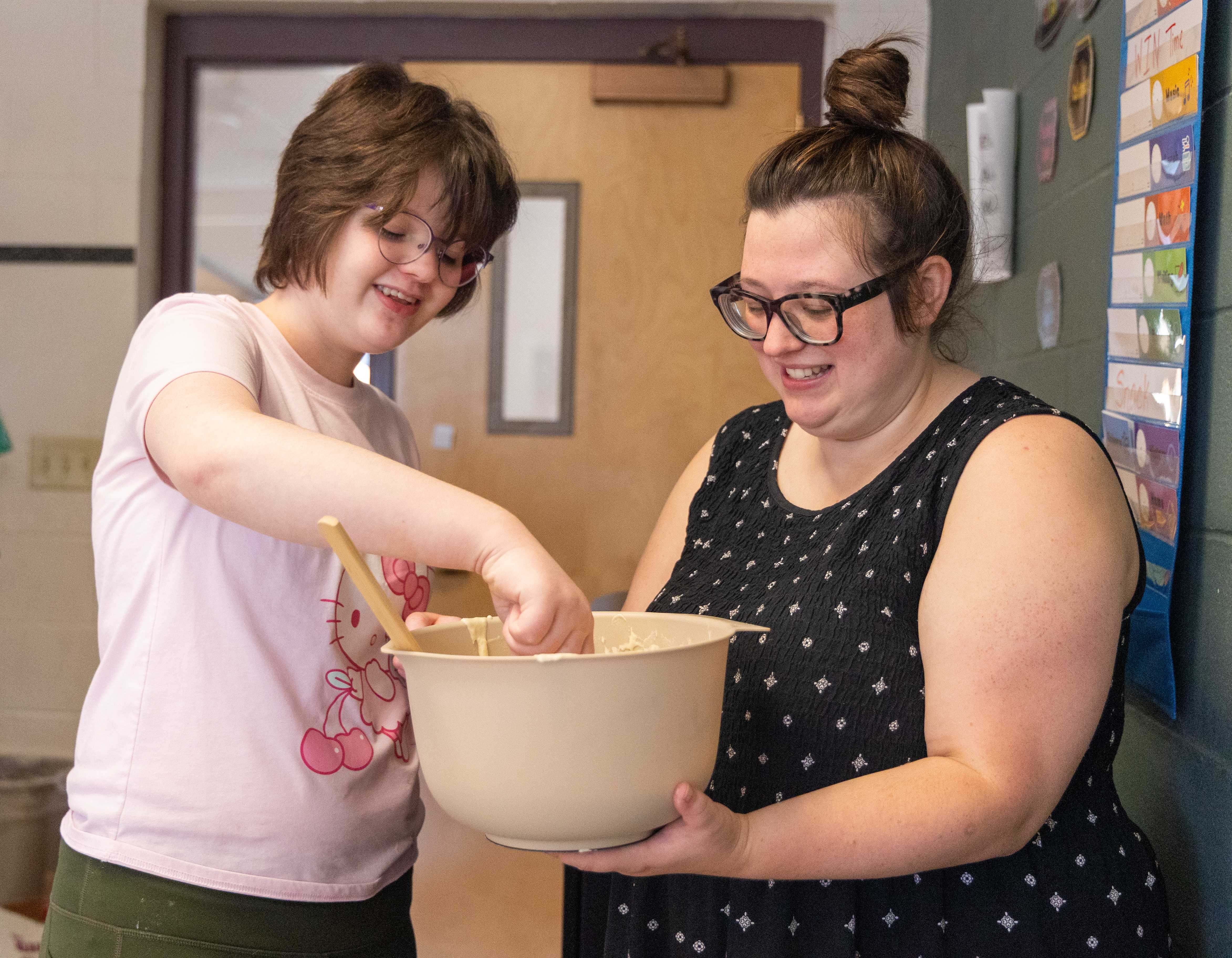 A teacher helps a student stir pancake batter in a bowl